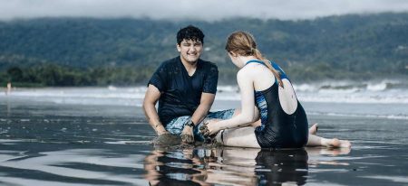 two people sitting in shallow water on the beach