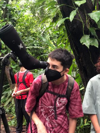 A student in the jungle in a mask looking through a scope