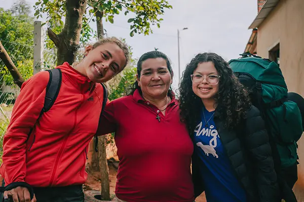 Two volunteers with backpacks posing warmly with their local host mother