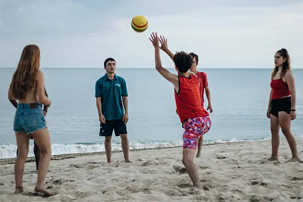 Group of young volunteers playing beach volleyball together by the ocean