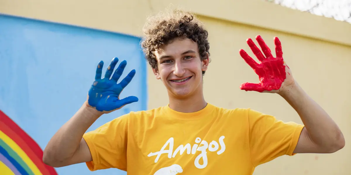 AMIGOS volunteer showing hands painted blue and red in front of a community mural