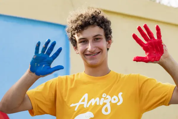 AMIGOS volunteer showing hands painted blue and red in front of a community mural