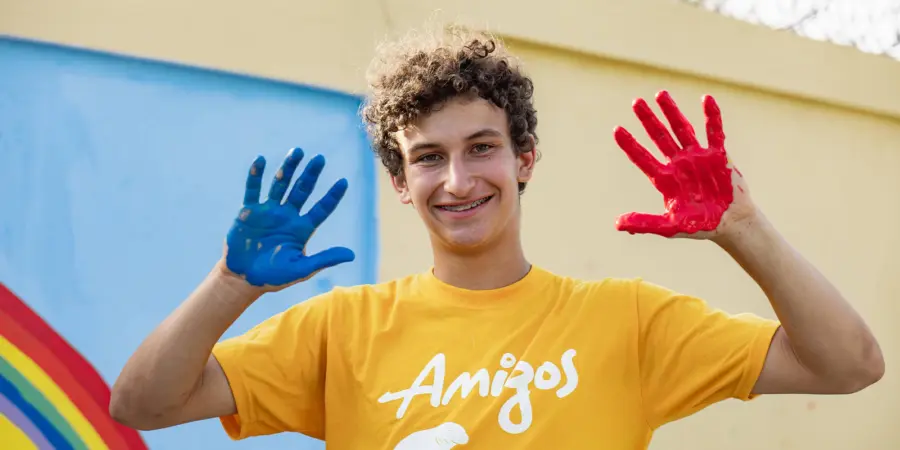 AMIGOS volunteer showing hands painted blue and red in front of a community mural