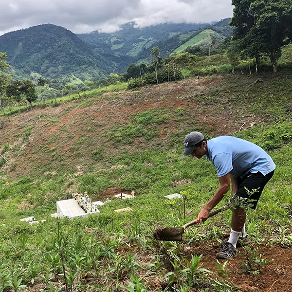 Local community member digging soil with a shovel on a hillside with mountain views