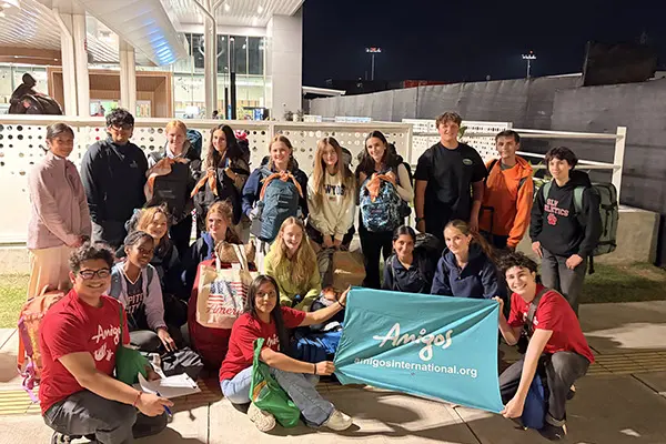 Group of AMIGOS volunteers posing with a banner outside the airport upon arrival