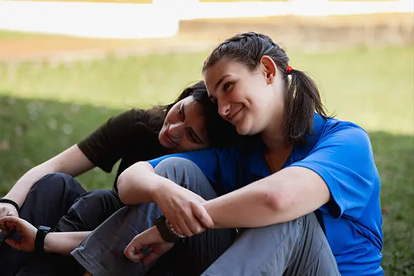 Two young volunteers sitting on the grass sharing a supportive moment during a debriefing session