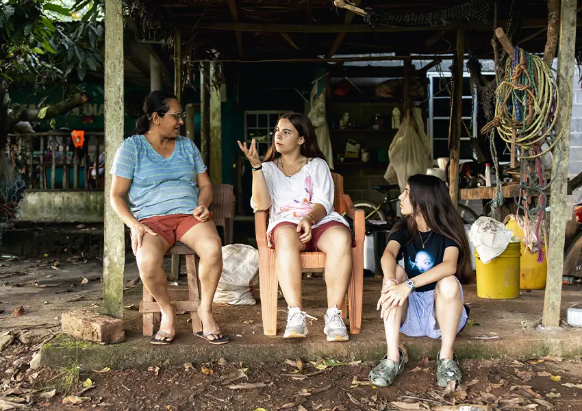 Volunteers sitting and conversing with their local host mother outside a home