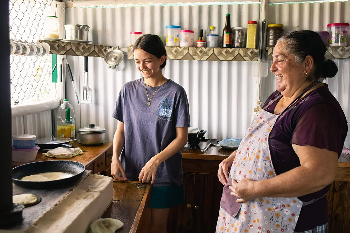 Volunteer and host mother smiling together while cooking in a home kitchen