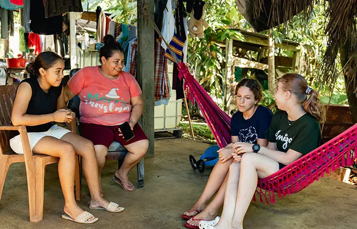 Voluntarios y miembros de familias anfitrionas relajándose y charlando bajo un patio con una hamaca