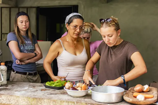 Host mother guiding volunteers as they slice vegetables in an outdoor kitchen