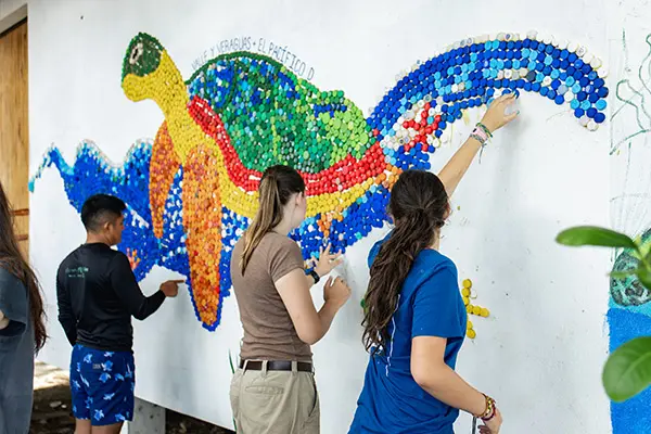 Volunteers working on a mural made of bottle caps