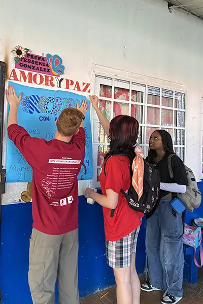 Volunteers taping up an activity poster outside a classroom