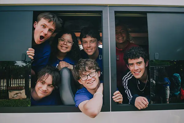 Group of cheerful young volunteers smiling out the windows of a travel van