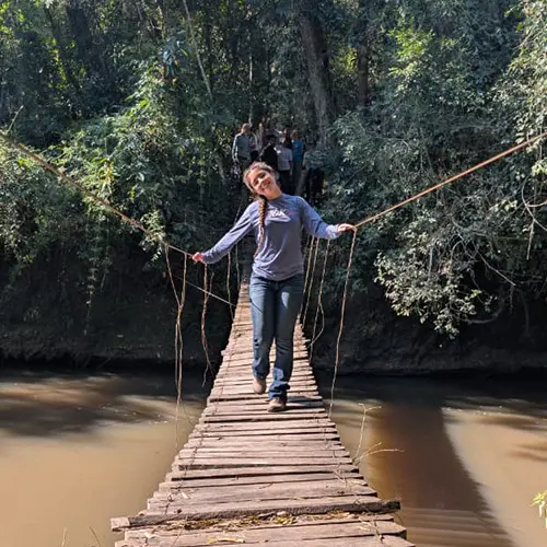Young volunteer smiling as she crosses a wooden suspension bridge over a river